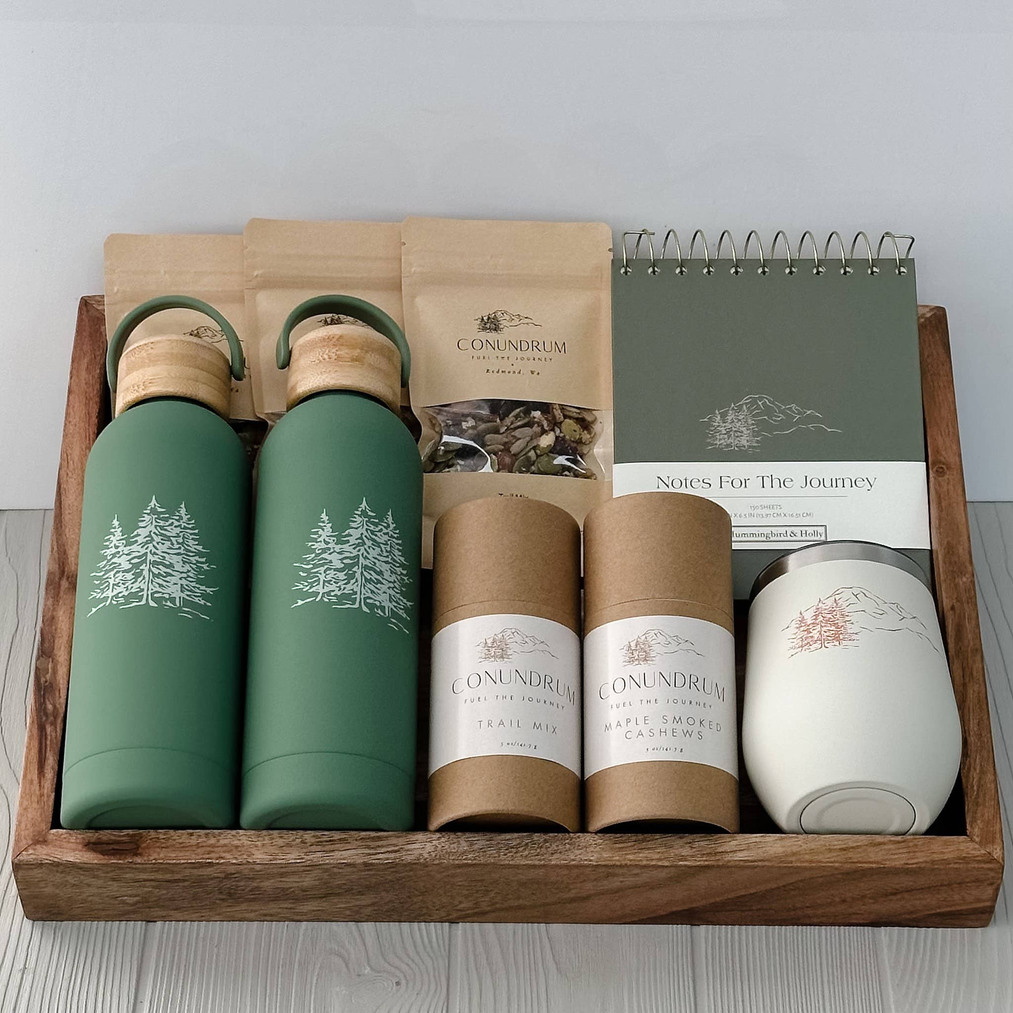 Gift set with green thermos bottles, Conundrum tea packages, and a candle in a wooden box.