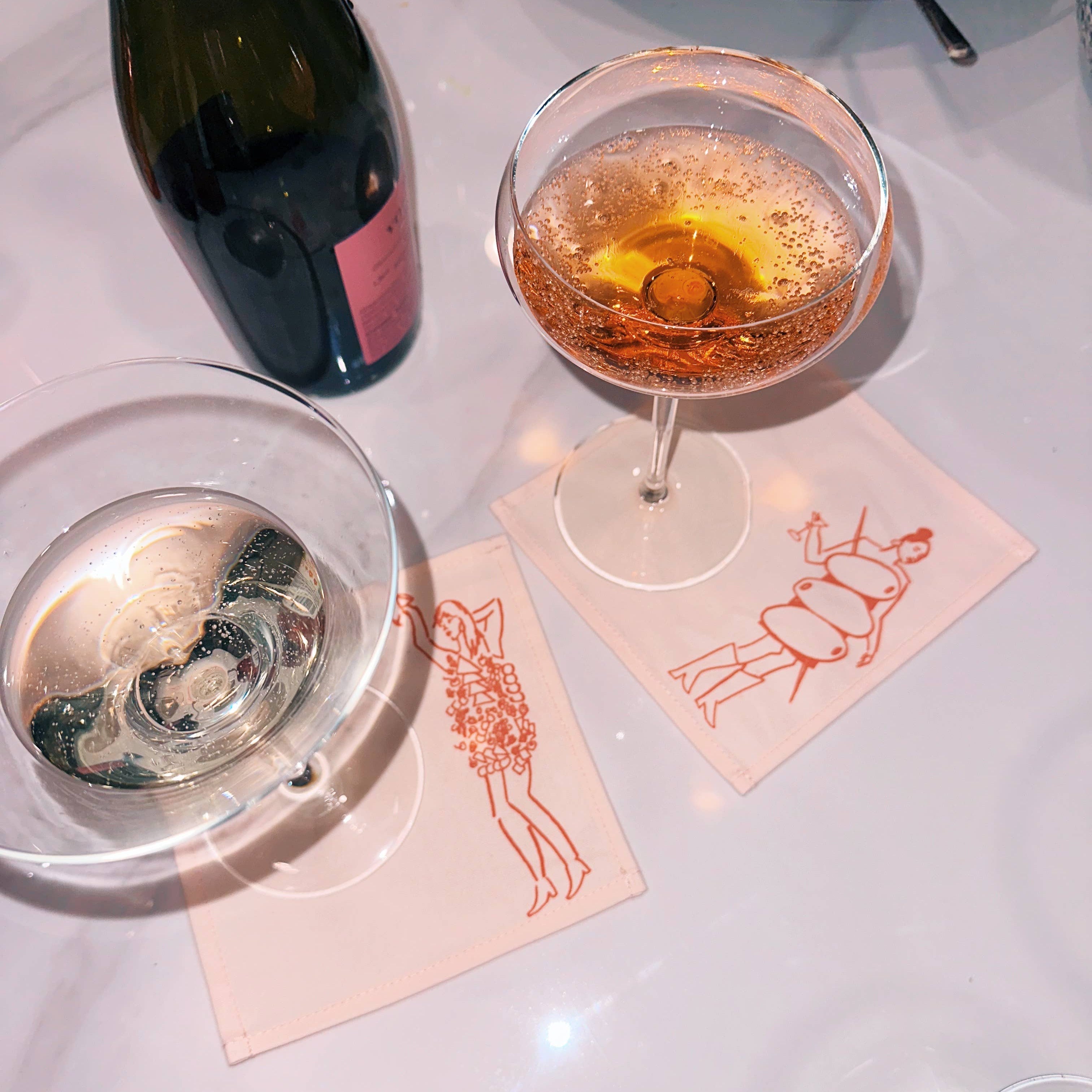 Two cocktail glasses with a bottle of champagne on a white table.