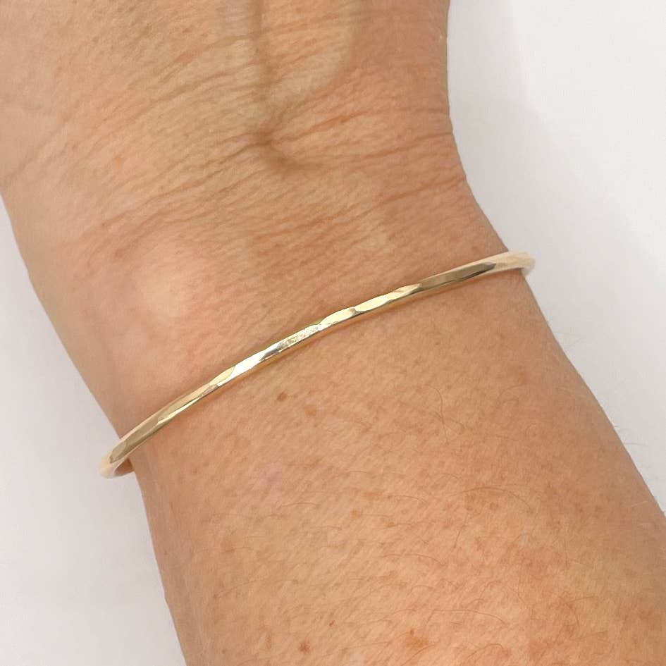Gold bracelet on a wrist against a white background