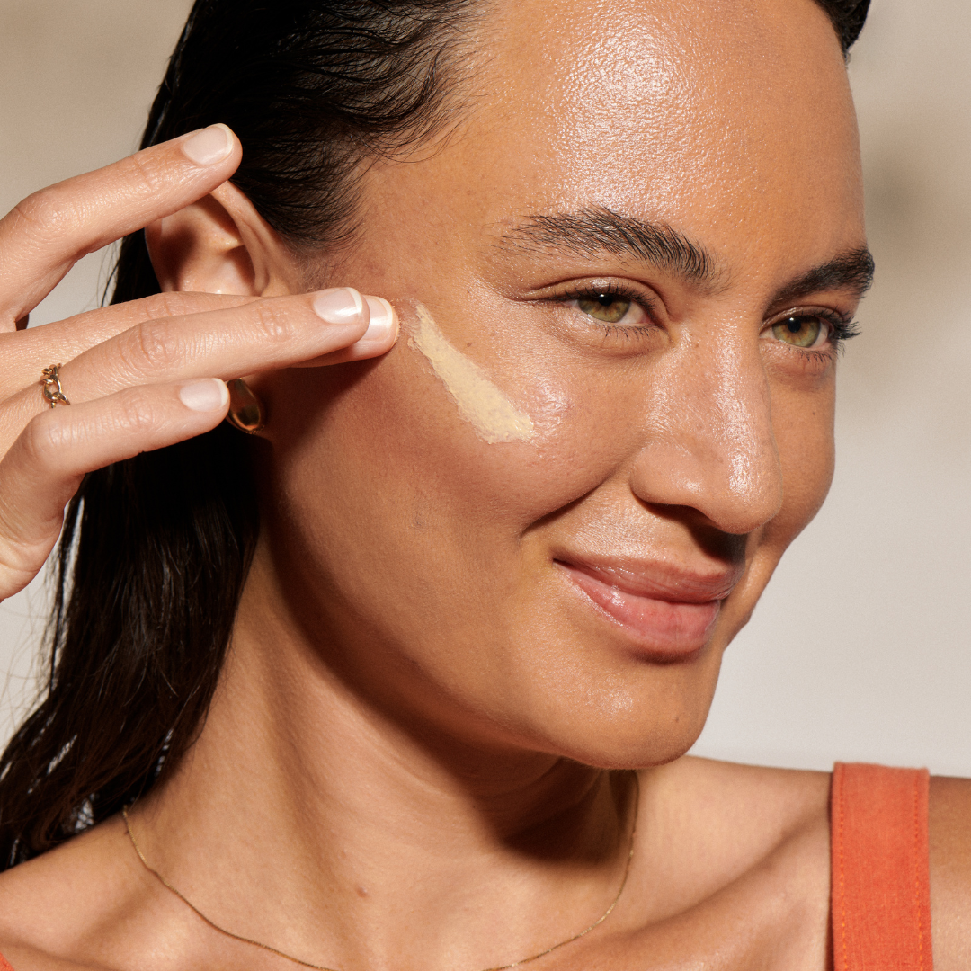 Woman applying a cosmetic product to her face with a neutral background