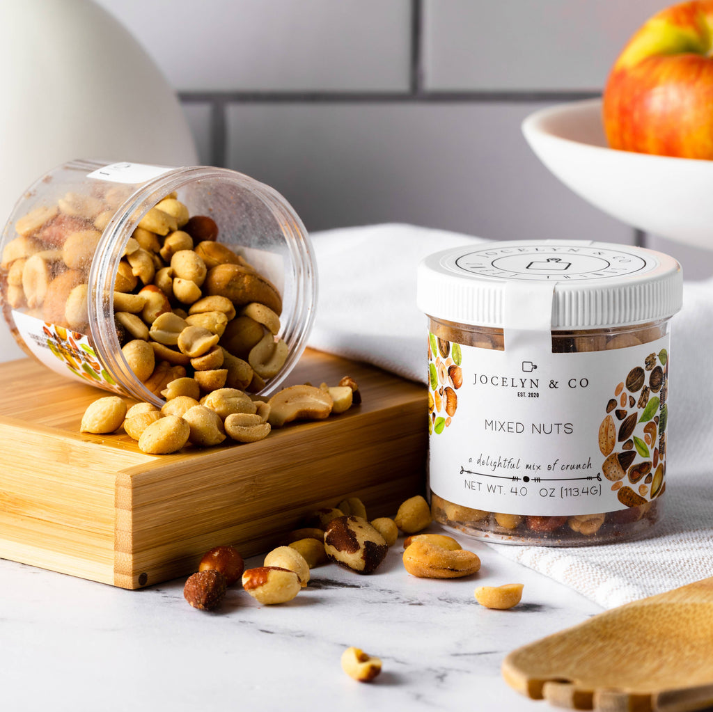 Jar of mixed nuts with a label on a marble surface, surrounded by nuts and an apple.