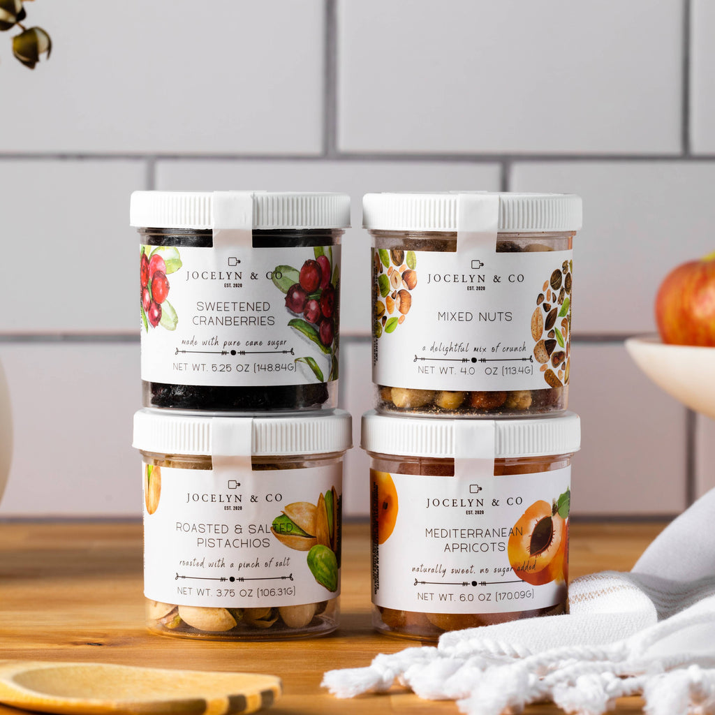 Four jars of Jocelyn & Co. snacks on a wooden surface with a kitchen background.