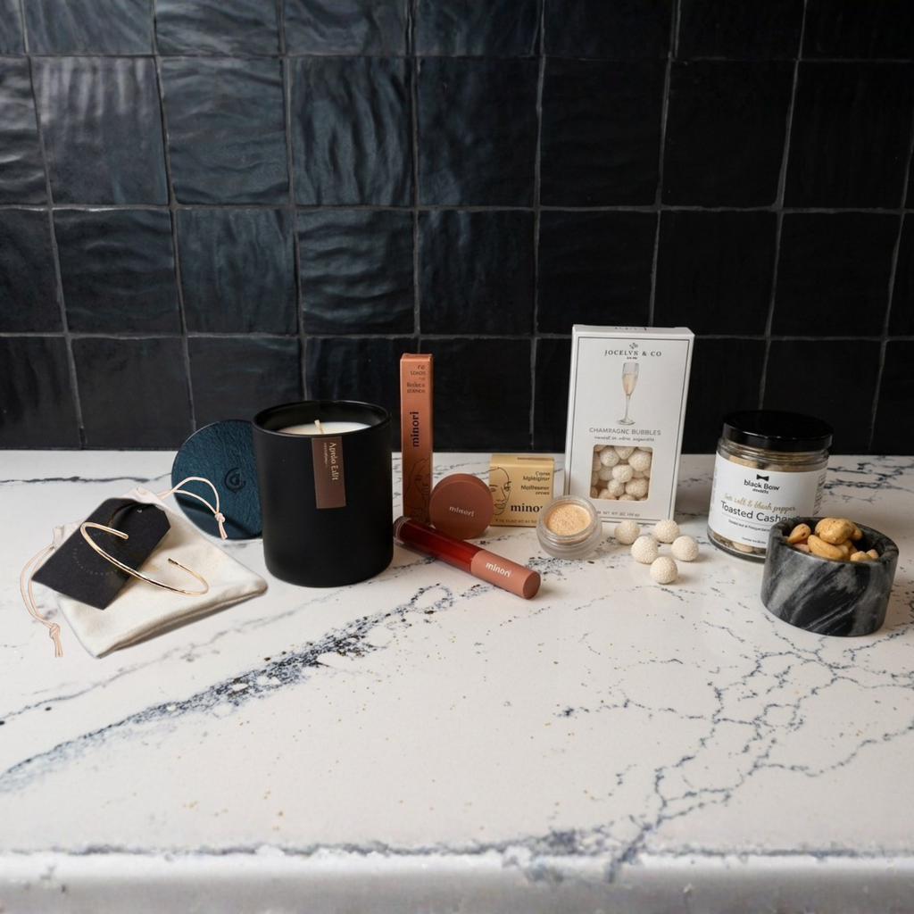 Candle, phone case, and other items on a marble countertop with a dark tiled wall in the background.