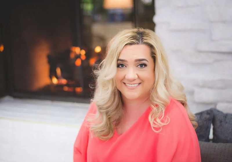 Debbie Quintana with blonde hair wearing a pink top in a cozy indoor setting.