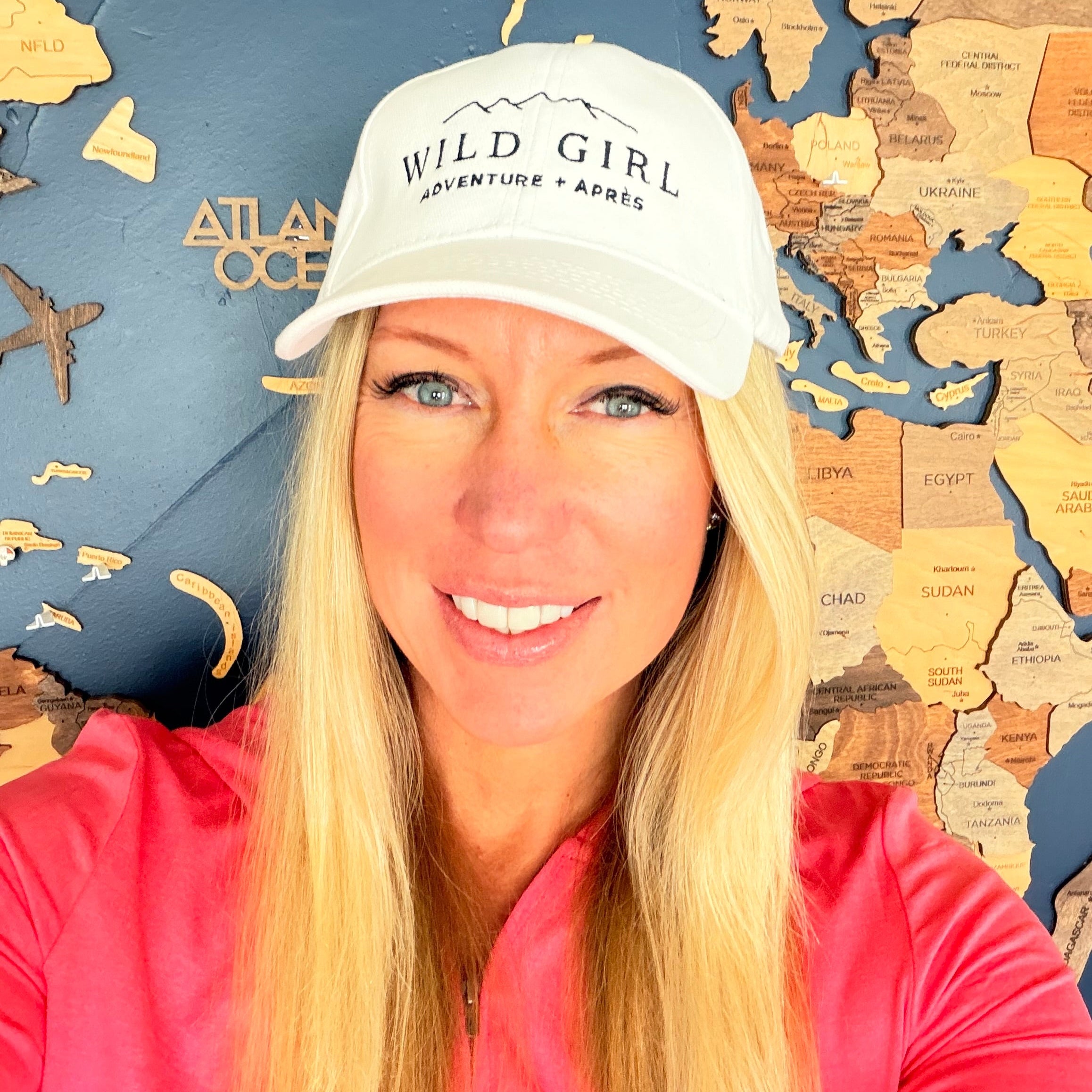 The Wild Girl wearing a 'Wild Girl Adventure + Après' cap in front of a world map