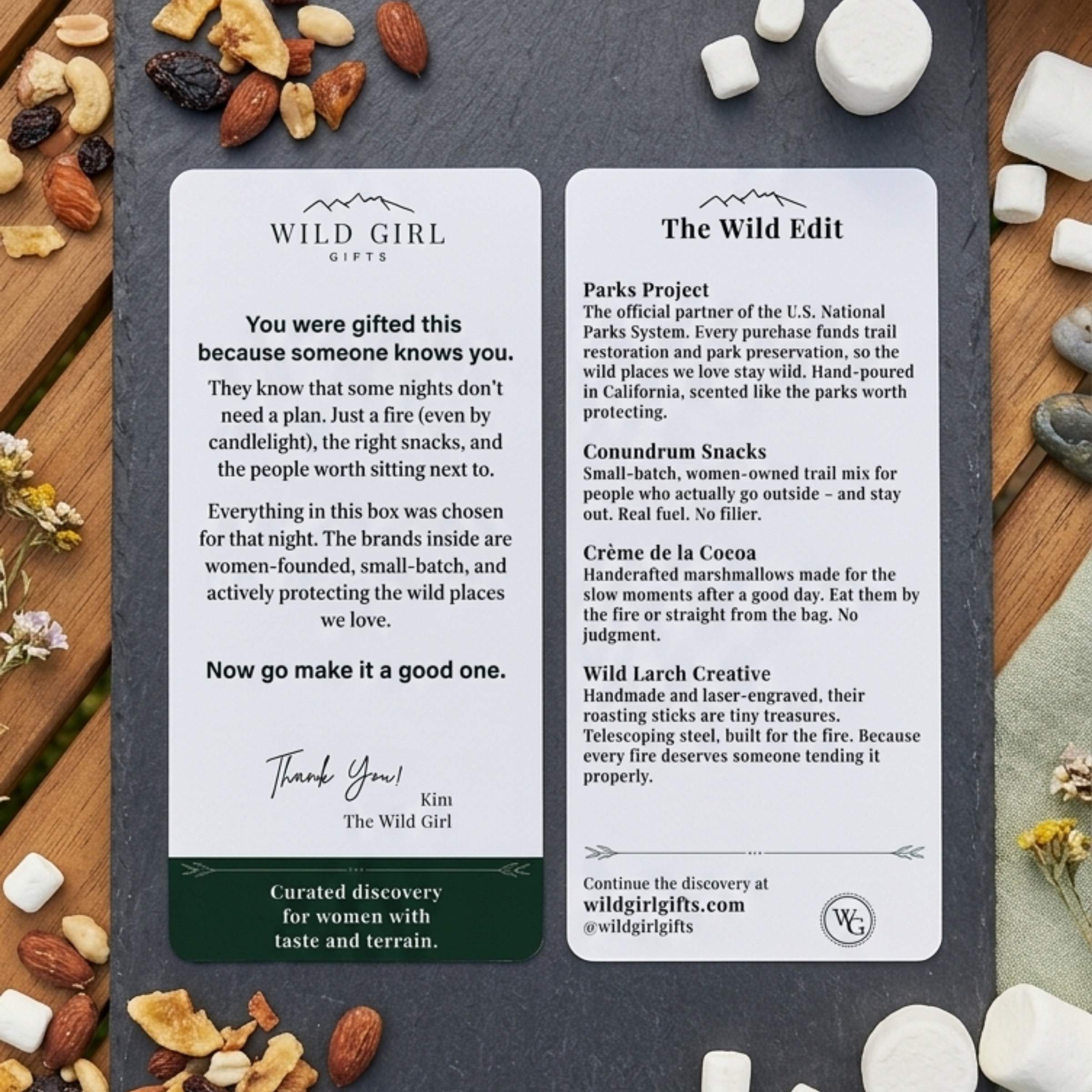 Two cards from Wild Girl Gifts with product descriptions on a wooden surface with snacks and marshmallows.