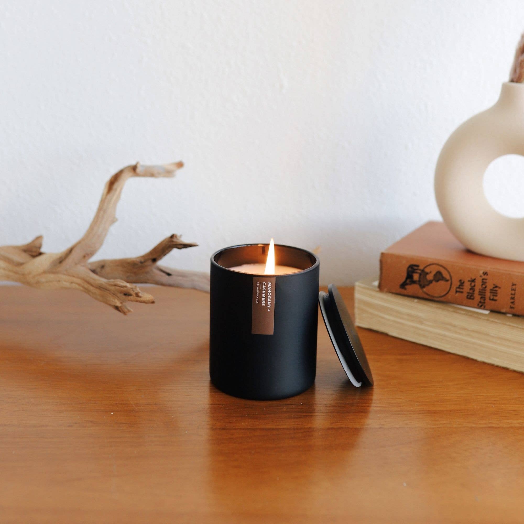 Black candle in a holder on a wooden surface with a white wall background