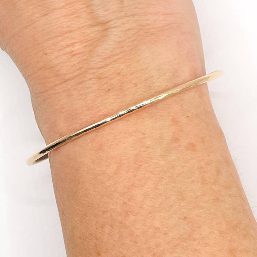 Gold bangle on a wrist against a white background