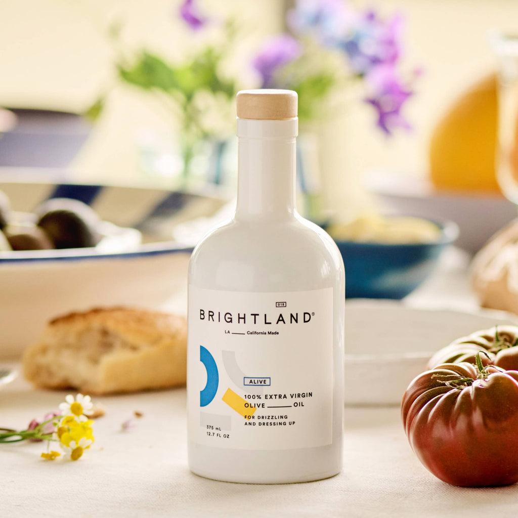 Bottle of Brightland olive oil on a table with food in the background