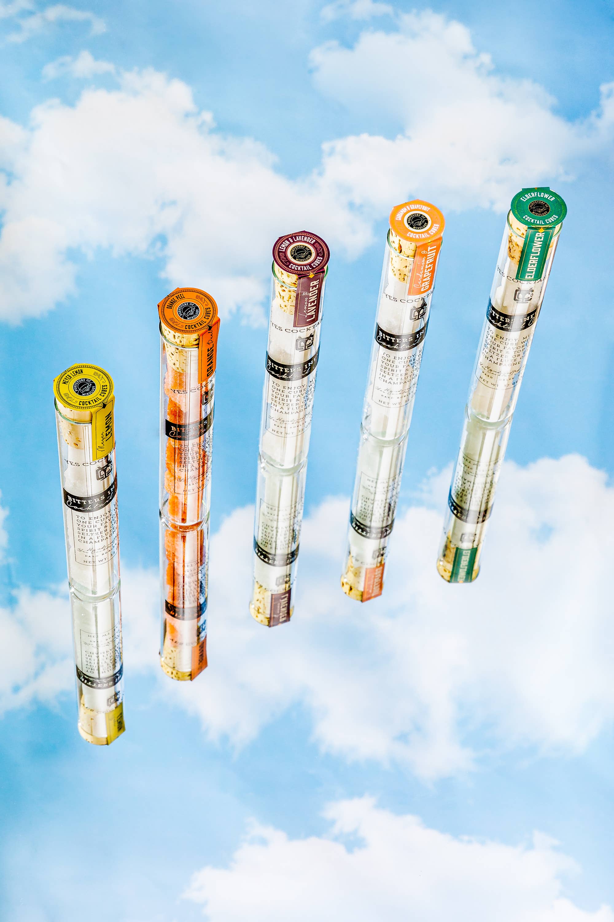Five cylindrical objects with colorful labels against a blue sky with clouds