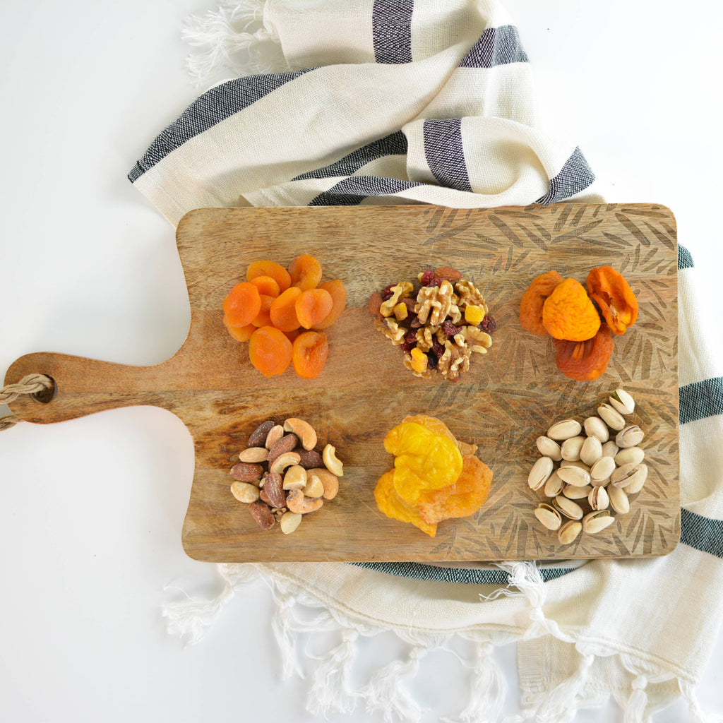 Wooden cutting board with dried fruits and nuts on a white background