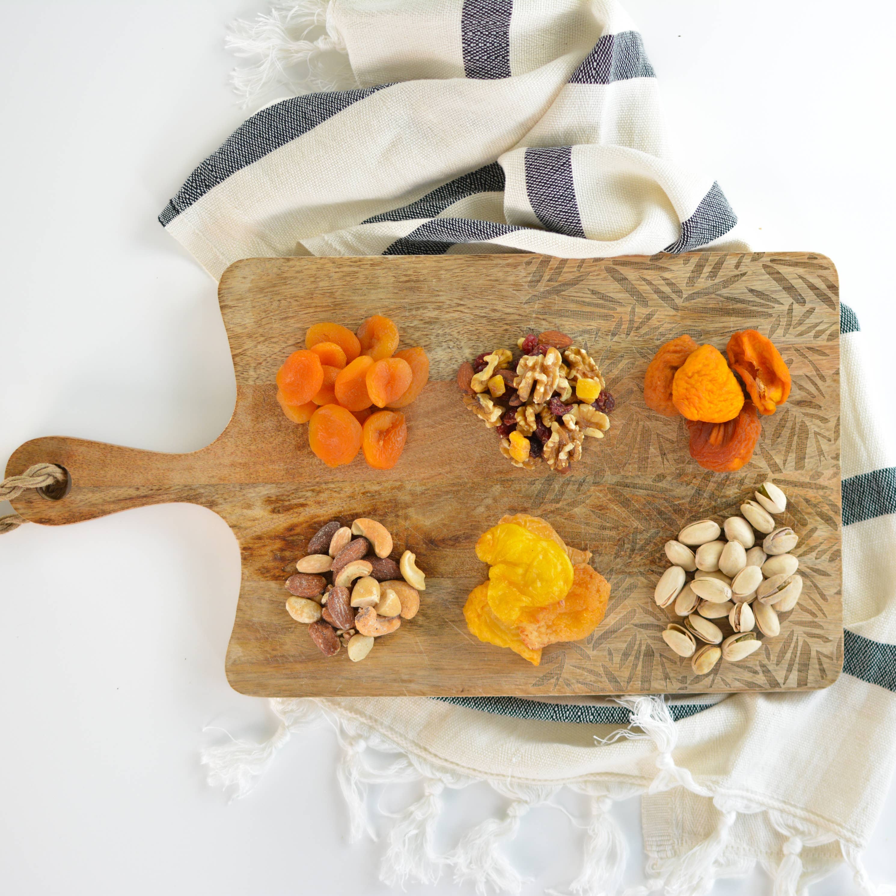 Wooden cutting board with dried fruits and nuts on a white background