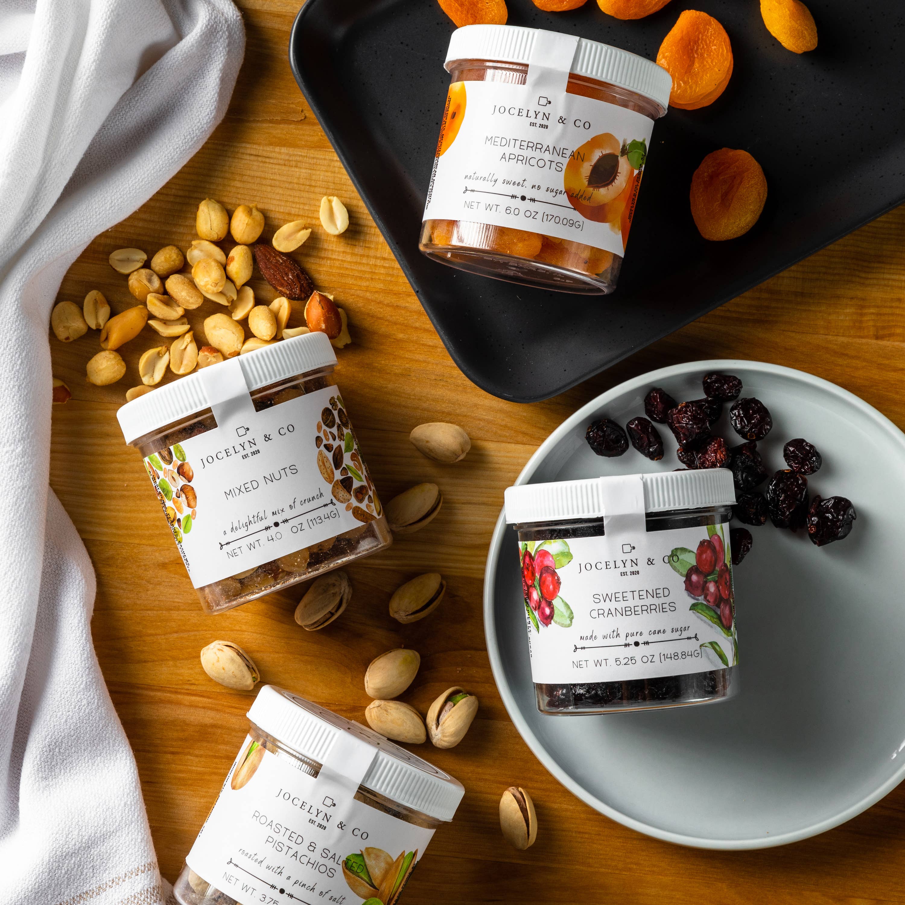 Jars of Jocelyn & Co. mixed nuts and dried fruits on a wooden surface.