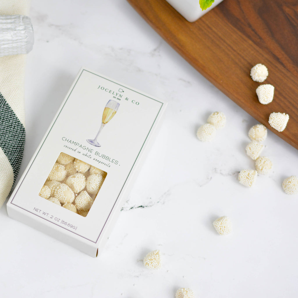 Box of champagne glass-shaped candies with a bottle of champagne and a plaid napkin on a white surface.