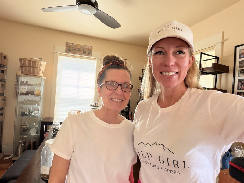 Kim with Gena of Salida Sunshine Botanicals in her Salida, Colorado workshop, shelves of tinctures and jars behind them.
