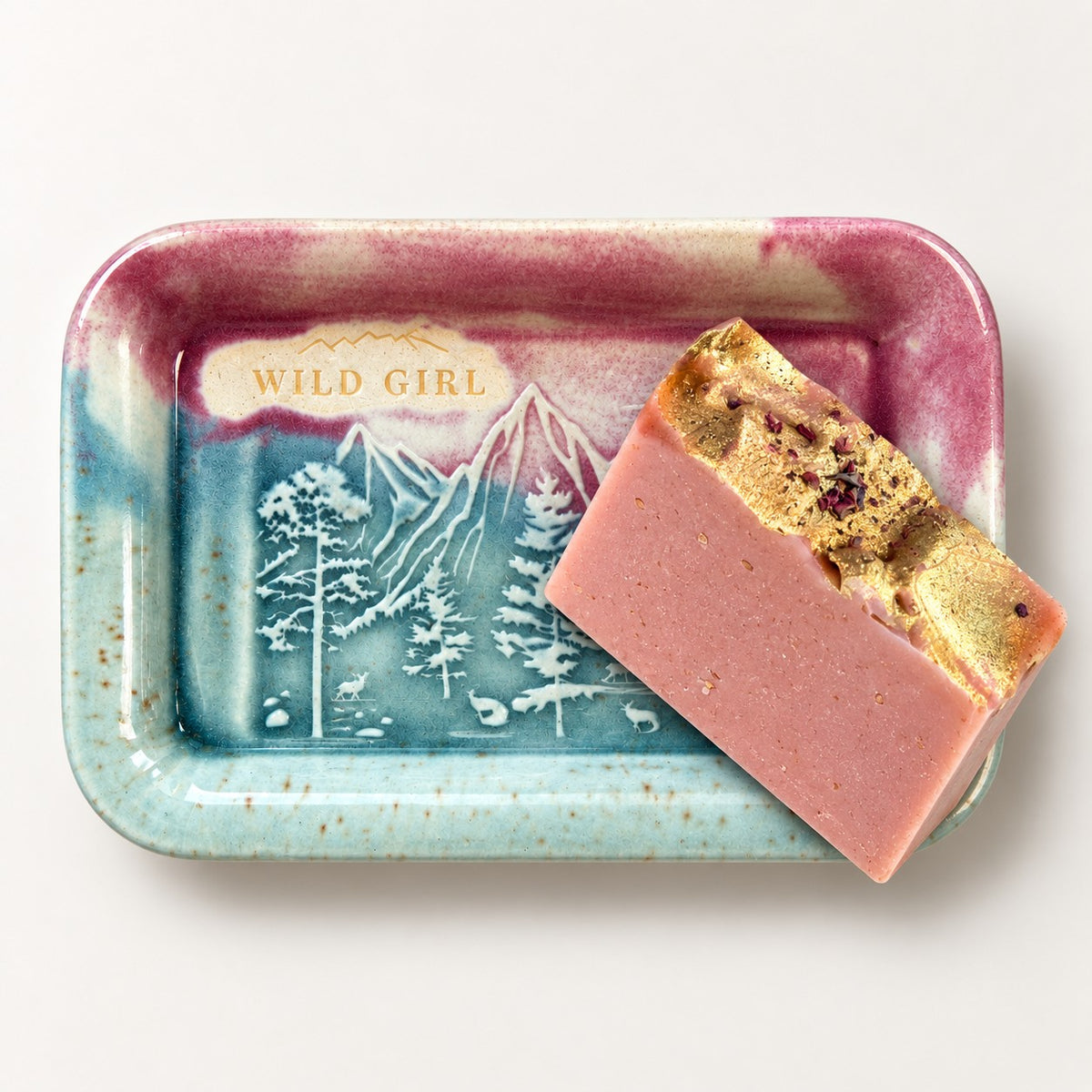 Wild Girl Sunrise Pink ceramic soap dish holding a pink Mountain Essentials Rose Gold goat's milk soap bar topped with gold leaf and dried rose petals.